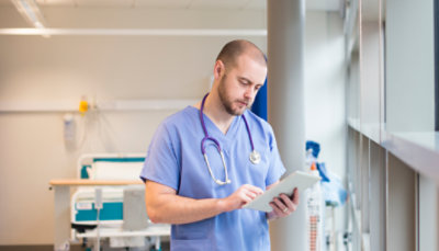 Professionnel de santé se tenant près d’une fenêtre et consultant une tablette 