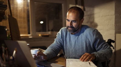 A person sitting at a desk using a laptop and reviewing paperwork
