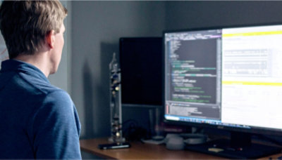 Computersoftwareprogrammierer, der auf zwei Bildschirme sieht.