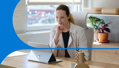 Nainen, joka istuu työpöydän ääressä ja työskentelee Microsoft Surface -tietokoneella.