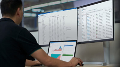 A person working at their desk on a laptop and two desktop monitors