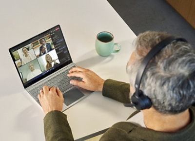 Eine Person, die ein Headset trägt und über ihren Laptop an einem Teams-Videoanruf teilnimmt