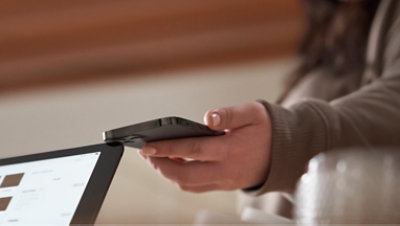 A man holding a mobile phone in his hand next to a laptop screen