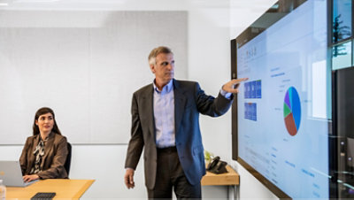 A man giving a presentation on a big screen in a conference room