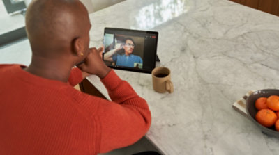 A person sitting at a kitchen counter and participating in a Teams video call on a tablet