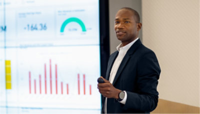 A person giving a presentation in front of a large screen displaying data.