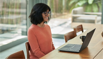 A person sitting at a table and smiling at their laptop.