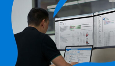 En person, der arbejder på en bærbar computer, der viser Outlook, og som er tilsluttet to skrivebordsskærme, der viser data