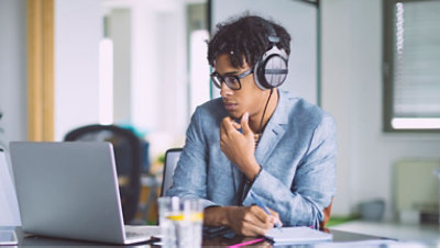 A person wearing headphones sits in a chair while using a laptop