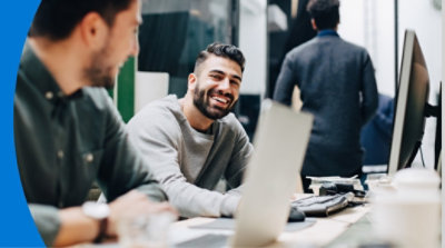Two people having a conversation at their desks next to each other.