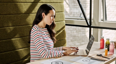 A person using a touchscreen desktop monitor while holding a mobile phone.