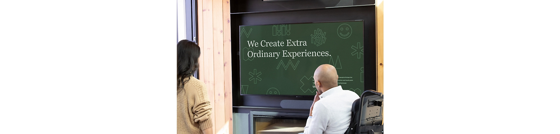 Two people in a meeting room viewing a PowerPoint presentation titled We Create Extra Ordinary Experiences.