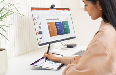 Eine Person, die mit Stift und Tablet Text zu einer PowerPoint-Präsentation hinzufügt, die auf einem Desktopmonitor angezeigt wird