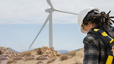 Personne portant un équipement de protection et qui se tient debout dans un champ avec des éoliennes.