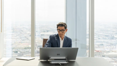 Persona strādā pie galda ar lielu skārienekrāna monitoru debesskrāpī