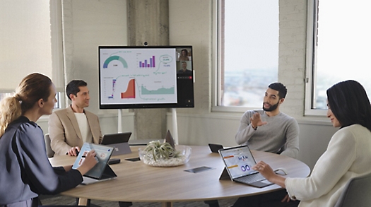 Four people in a meeting sitting around a circular table while a PowerPoint presentation is being given over a Teams call