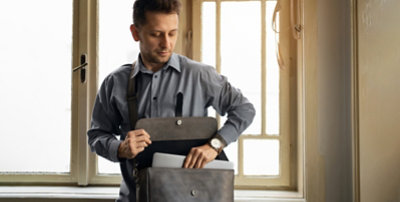 A person pulling a laptop out of a crossbody bag they are wearing.