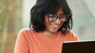 A woman wearing glasses is smiling and using laptop