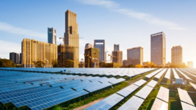 A field of solar panels and a city skyline in the distance.