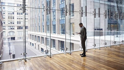 A person standing in front of a wall of windows looking at a mobile phone