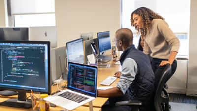 A team collaborates around computers in an office, with code visible on several monitors.