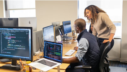 A team collaborates around computers in an office, with code visible on several monitors.