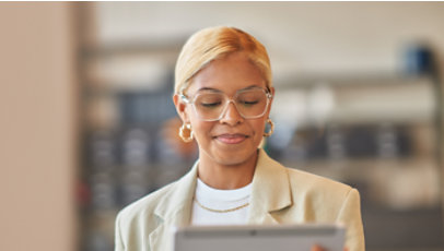 A professional wearing clear-framed glasses looks down at a tablet in an office.