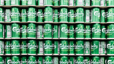 Rows of green Carlsberg Denmark cans are stacked tightly on store shelves.