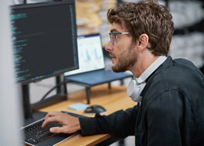 A person with long hair, wearing a black shirt, sits on a couch focused on writing 