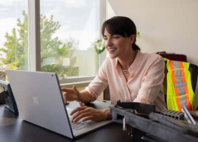 A woman in a pink shirt sitting at a desk using a laptop.