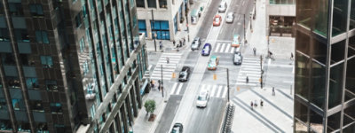 Straatweergave in een stad vanuit een hoge hoek in een kantoorgebouw. Auto's die over een kruising rijden naar een eenrichtingsweg. Enkele voetgangers die zichtbaar zijn op de stoep en een zebrapad.