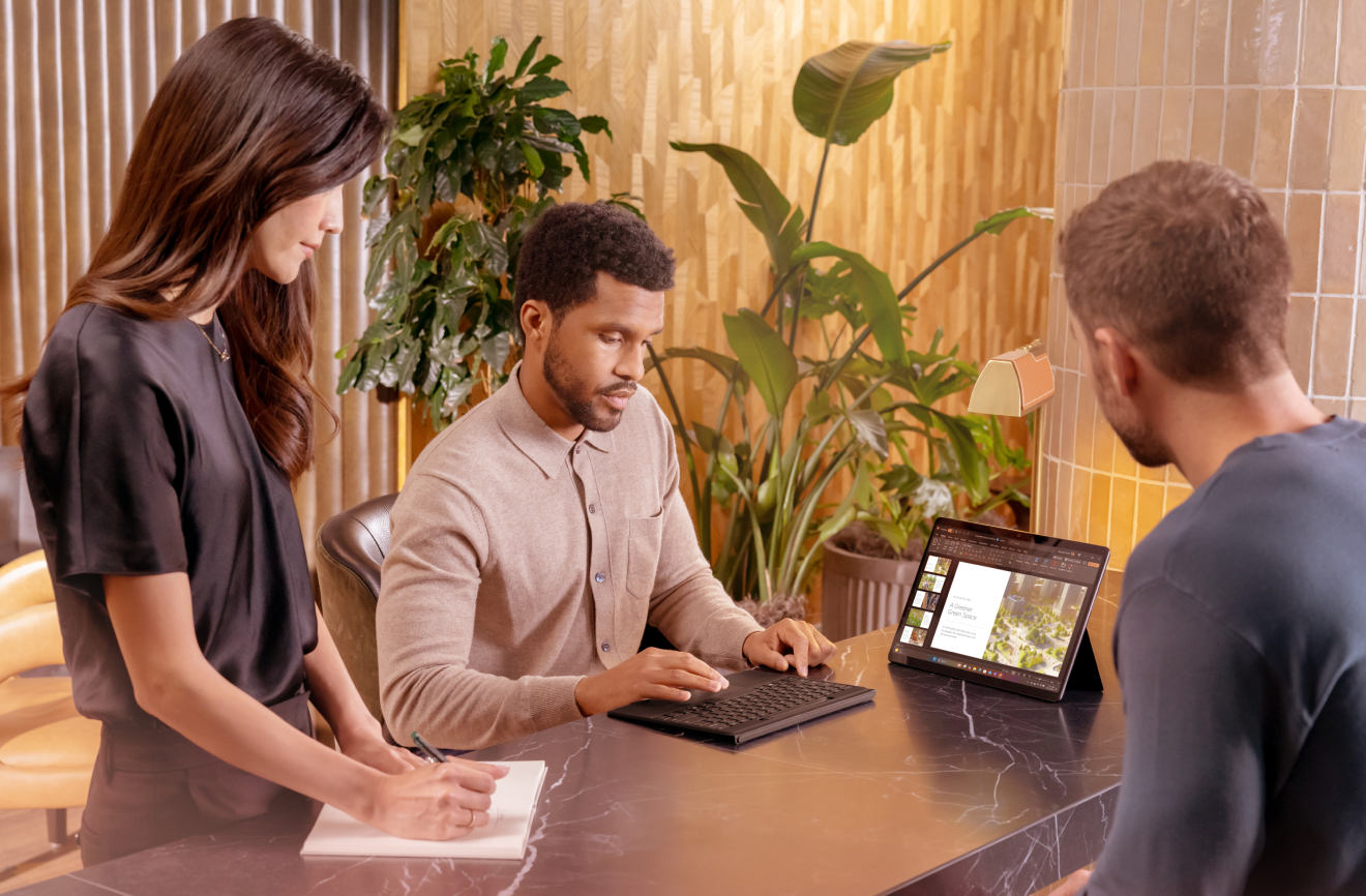 Three professionals around a table looking at Copilot + PowerPoint on a Surface