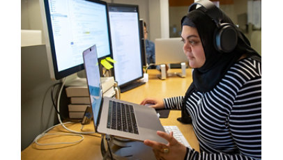 Female developer coding at her desk, wearing hijab and headphones.