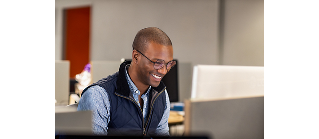 Een man glimlacht terwijl hij op een computer werkt.