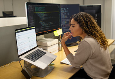 O persoană stând la birou cu un laptop și mai multe ecrane.