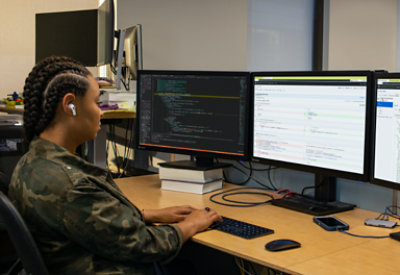 O persoană purtând căști și lucrând la birou cu mai multe monitoare.