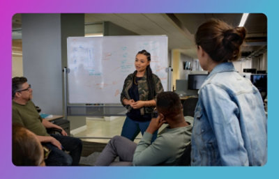 A woman standing in front of a whiteboard, presenting to her team.