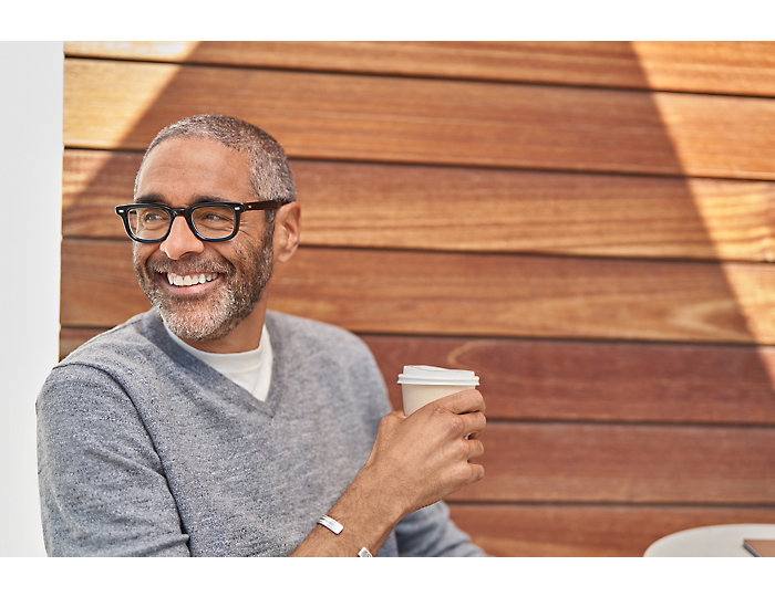 Uma pessoa usando óculos, segurando uma xícara e sorrindo.