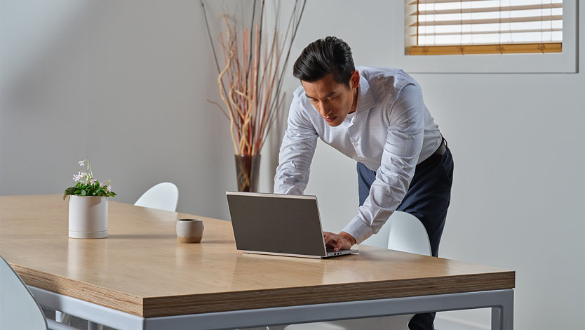 立ちながらテーブルで Surface デバイスを使用する人物。