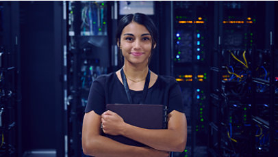 Female IT worker standing in a server room holding a folder and smiling.
