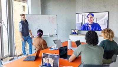 People meeting in conference room with remote attendees on screen