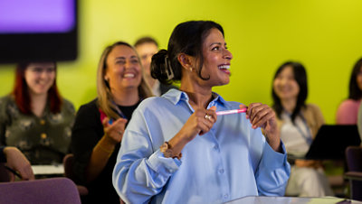 Woman in a classroom of adult students sits at a desk and smiles
