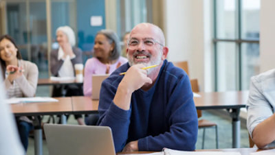 Smiling adult student engaged in a classroom with peers in the background.