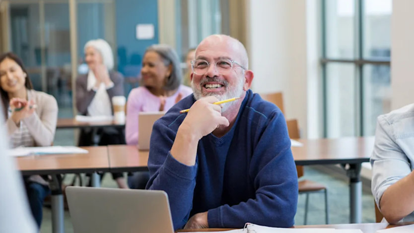 Smiling adult student engaged in a classroom with peers in the background.