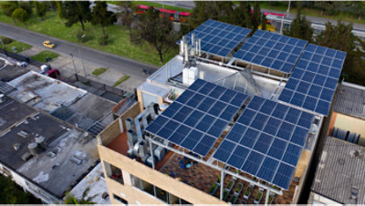 Rooftop covered with solar panels on a city building, with surrounding streets and trees visible from above.