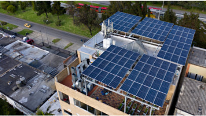Rooftop covered with solar panels on a city building, with surrounding streets and trees visible from above.