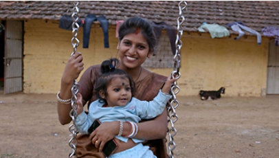 A smiling woman and child together on a swing in rural India.