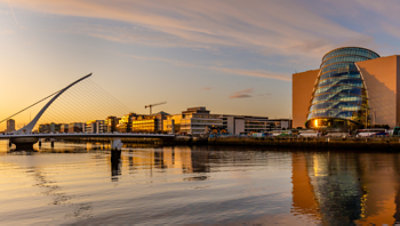 Modern waterfront view of Dublin at sunset, with the Samuel Beckett Bridge, River Liffey, and Convention Centre Dublin reflecting on the water.