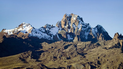 Snow-capped mountain peaks rising above a rocky landscape under a clear blue sky.