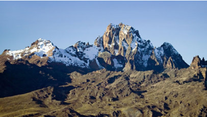 Snow-capped mountain peaks rising above a rocky landscape under a clear blue sky.